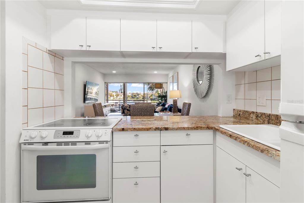 A white kitchen with granite countertops overlooks a living area with a view of water — 4340 FALMOUTH DRIVE UNIT D-204, LONGBOAT KEY, FL