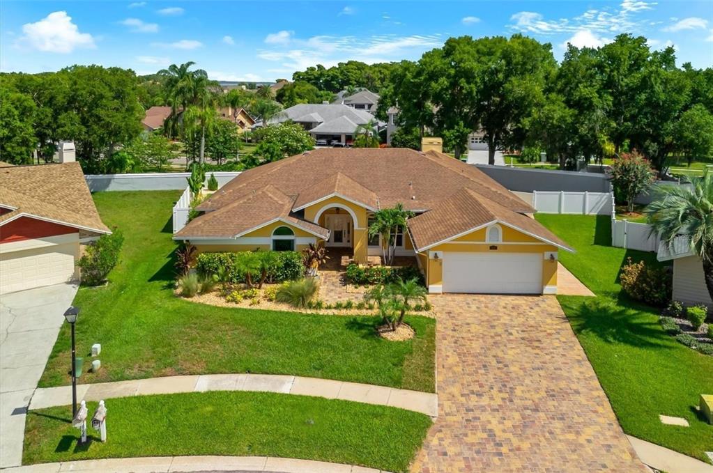 An aerial view of a yellow single-story house with a brown roof and paver driveway — 1874 STABLE TRAIL, PALM HARBOR, FL