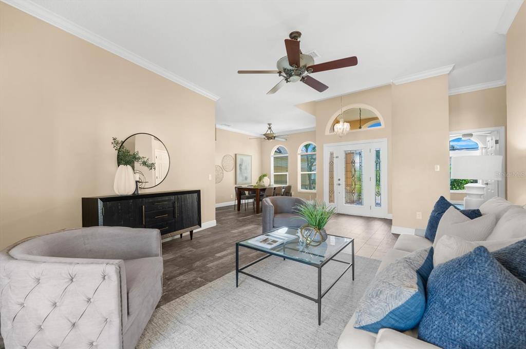 A living room with a glass coffee table, gray armchairs, and a dining area beyond — 1874 STABLE TRAIL, PALM HARBOR, FL