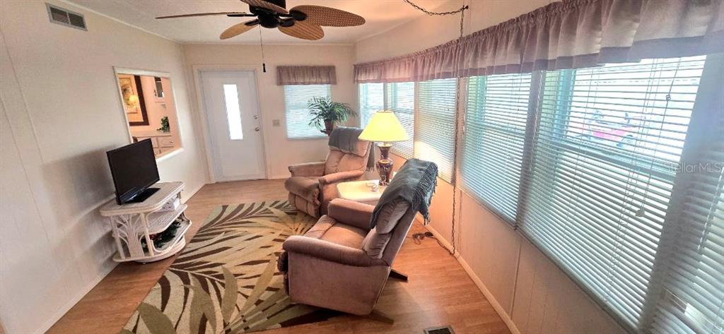 A sunroom features a ceiling fan, two armchairs, a television, and large windows with blinds — 40 CONCORD LANE, PALM HARBOR, FL