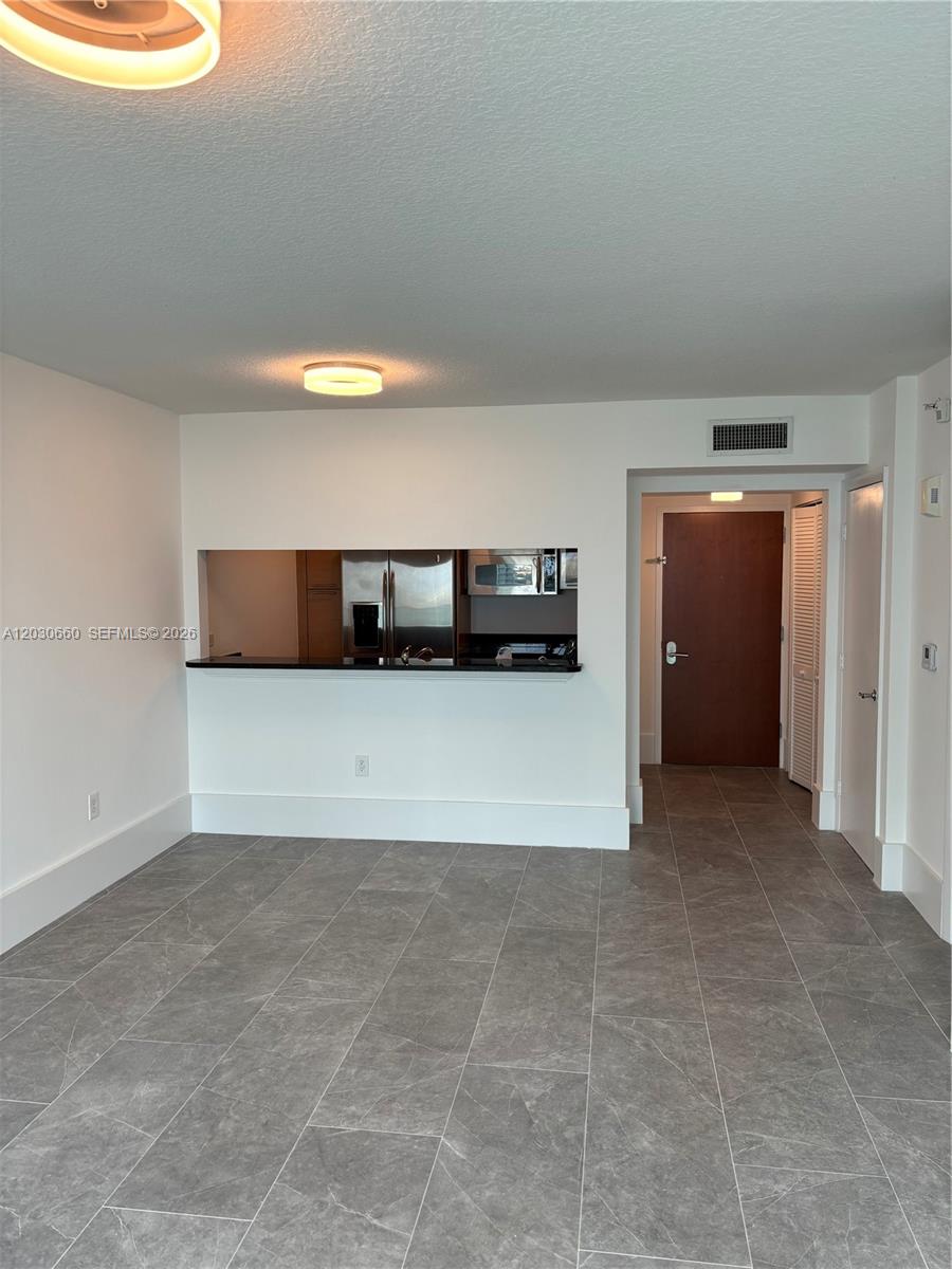 A room with gray tile flooring features a kitchen pass-through window and white walls — 31 SE 5th St # 2103, Miami FL 33131, MIAMI, FL