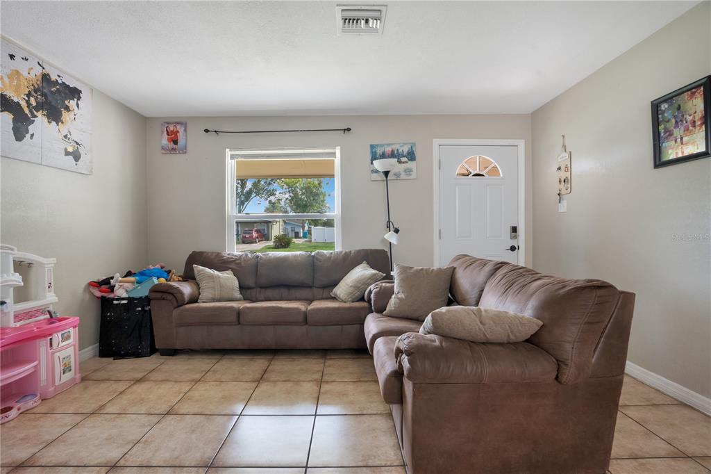 A living room features a brown sectional sofa, tile flooring, and a front door — 4325 CASSIUS STREET, ORLANDO, FL