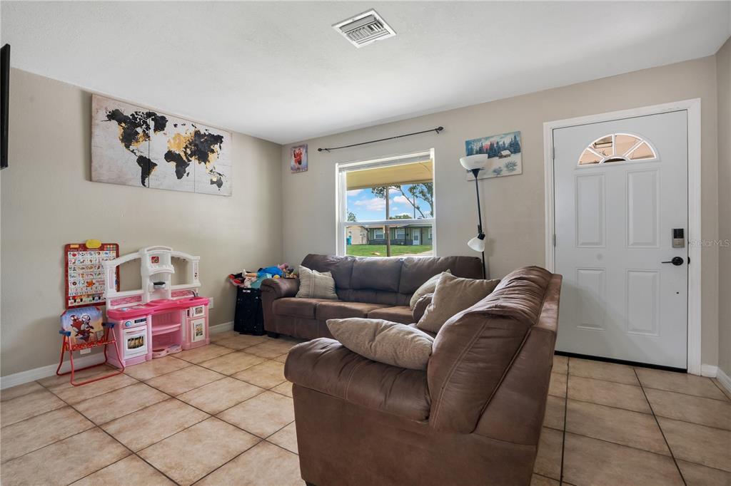 A living room features beige walls, tile flooring, a brown sectional sofa, and a front door — 4325 CASSIUS STREET, ORLANDO, FL
