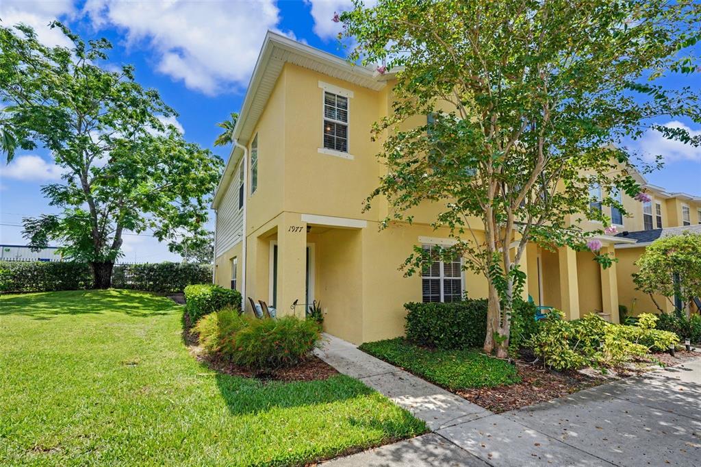 A two-story yellow stucco townhouse with a front entrance and a small landscaped yard — 1977 SEARAY SHORE DRIVE, CLEARWATER, FL