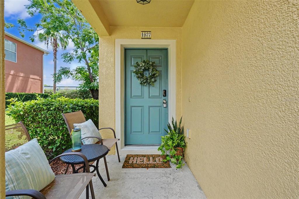 A covered front porch features a blue door, patio furniture, and a welcome mat — 1977 SEARAY SHORE DRIVE, CLEARWATER, FL