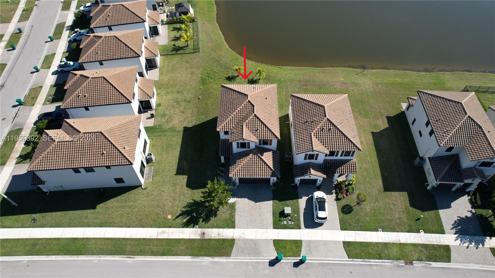 An aerial view shows a two-story house with a tiled roof next to a lake — 5632 Cerva LN, Ave Maria FL 34142, AVE MARIA, FL