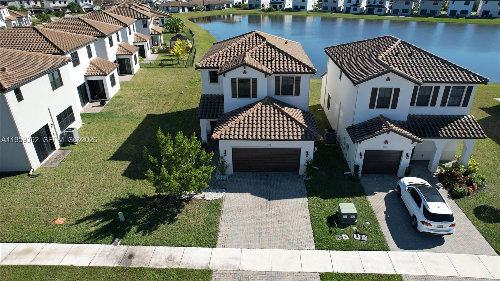 An aerial view shows two-story suburban houses with tile roofs and paved driveways near a lake — 5632 Cerva LN, Ave Maria FL 34142, AVE MARIA, FL