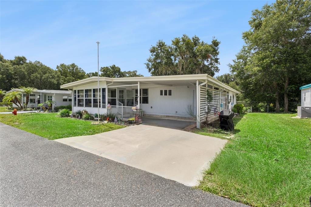 A single-story manufactured home with a concrete driveway, carport, and screened-in front porch — 104 OLEANDER COVE, LEESBURG, FL
