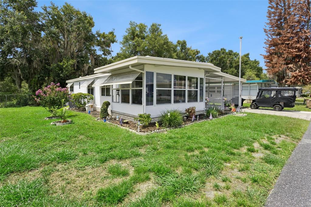 A single-story manufactured home with a white exterior, large windows, and a covered carport — 104 OLEANDER COVE, LEESBURG, FL