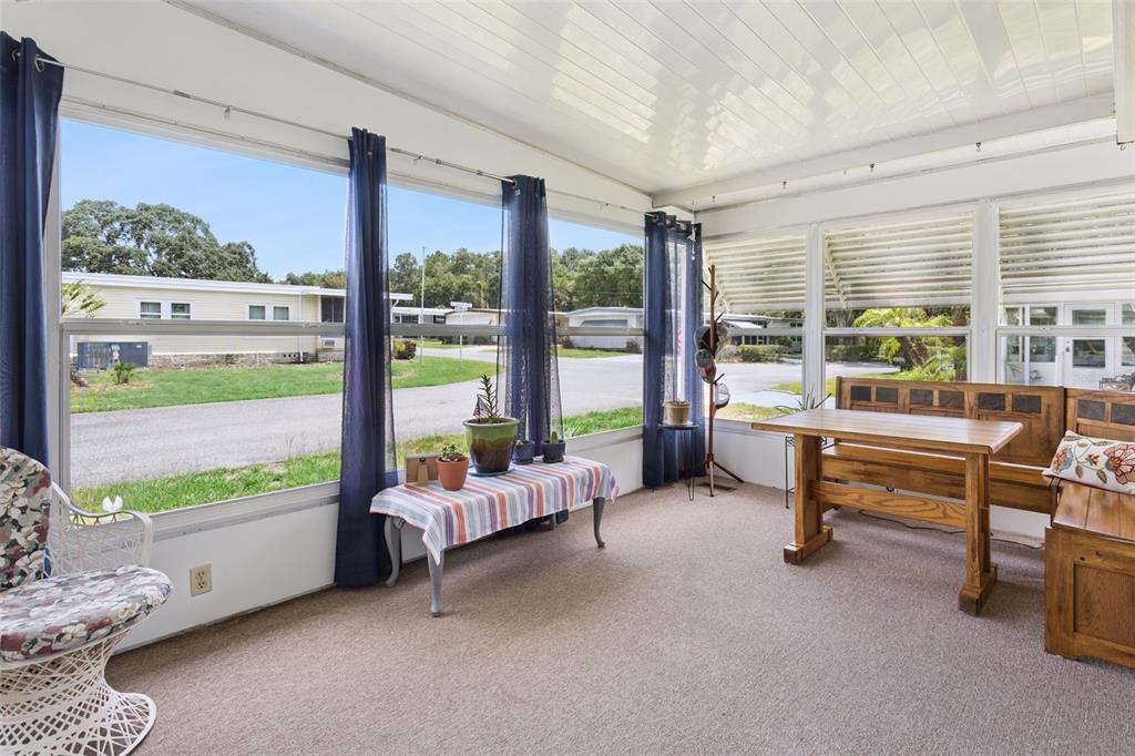 A sunroom features carpeted floors, large windows with blue curtains, and a wooden dining set — 104 OLEANDER COVE, LEESBURG, FL