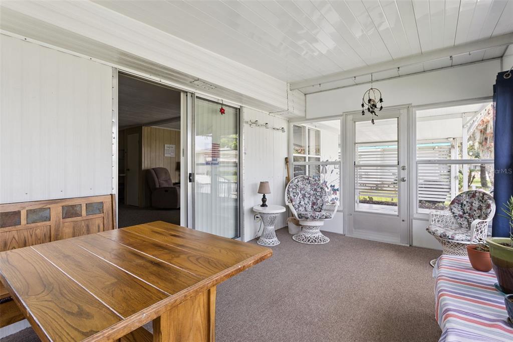 A sunroom features a wooden table, wicker chairs, carpeted flooring, and a sliding glass door — 104 OLEANDER COVE, LEESBURG, FL