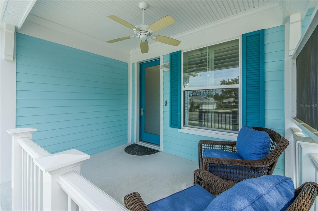 A covered porch features light blue horizontal siding, a ceiling fan, and two wicker chairs — 357 CONCH KEY LANE, LADY LAKE, FL