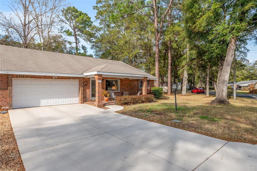 A brick house with a white garage door and a concrete driveway sits among trees — 8707 SW 88TH COURT ROAD UNIT K, OCALA, FL
