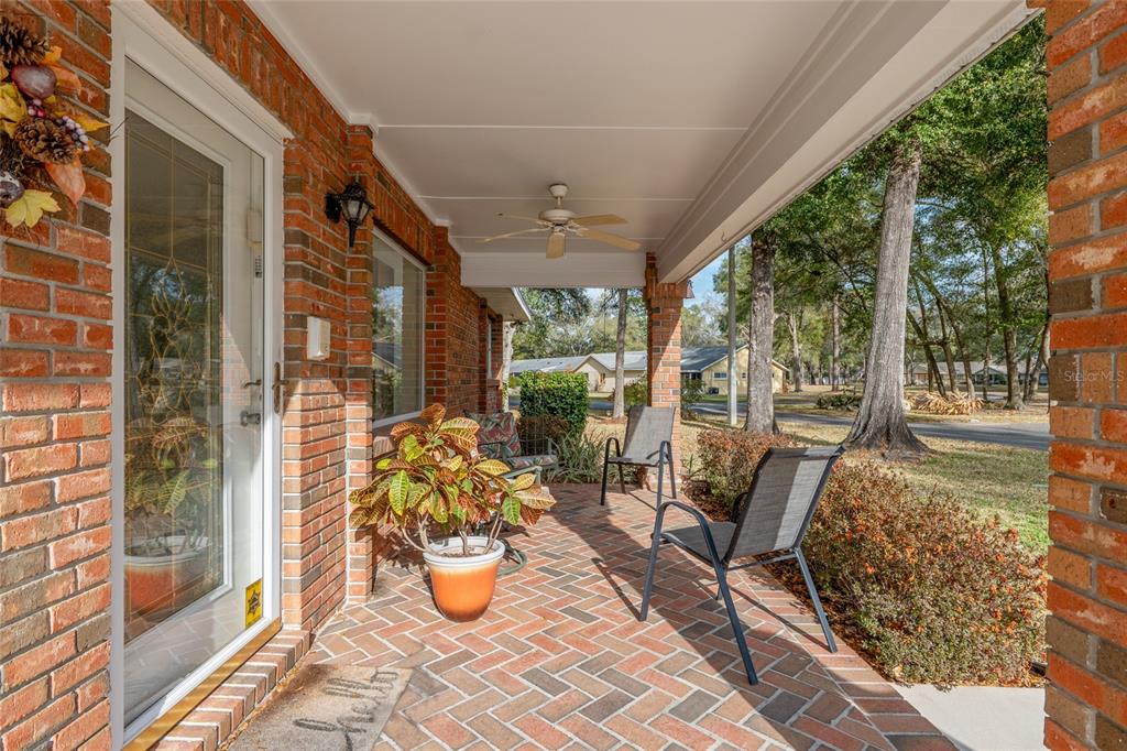 A covered brick porch features a ceiling fan, outdoor seating, and a front door — 8707 SW 88TH COURT ROAD UNIT K, OCALA, FL