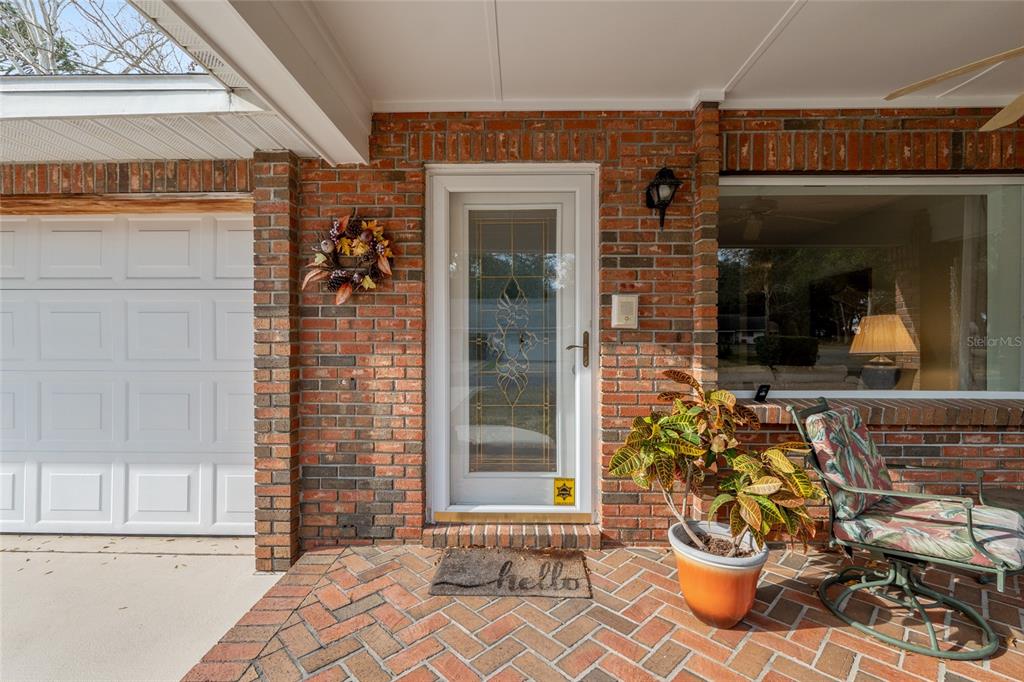 A brick-front home features a white storm door, a potted plant, and a patio chair — 8707 SW 88TH COURT ROAD UNIT K, OCALA, FL