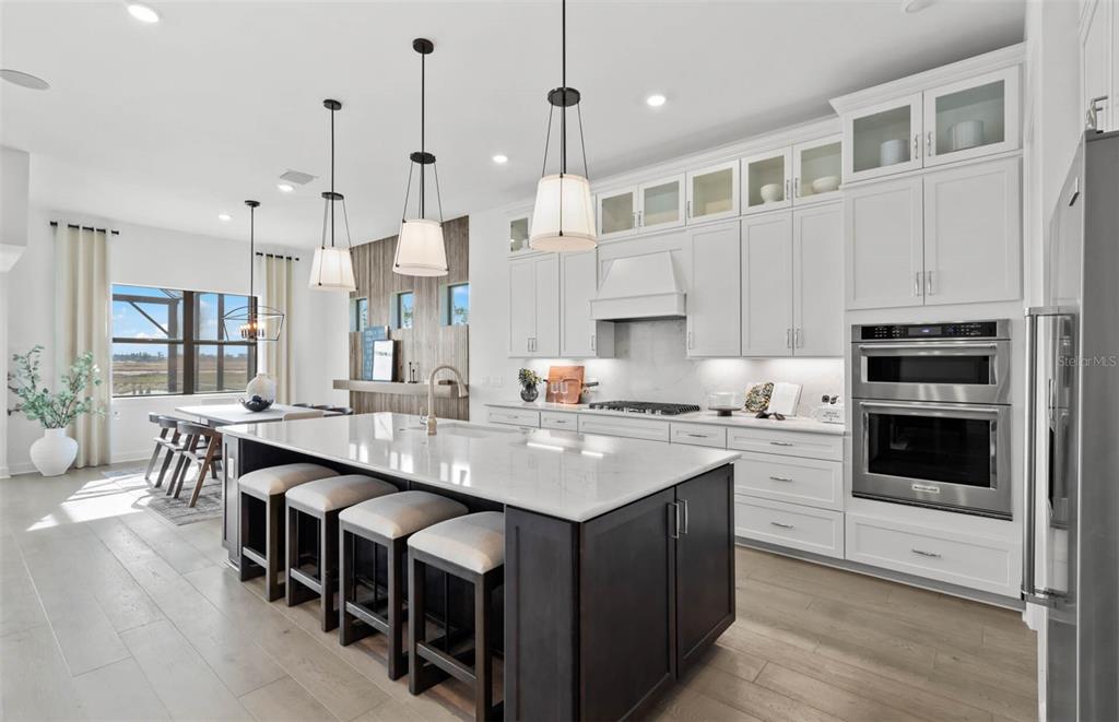 A modern kitchen features a dark wood island, white cabinetry, stainless steel appliances, and pendant lighting — 4933 DEL REY COVE, LAKEWOOD RANCH, FL