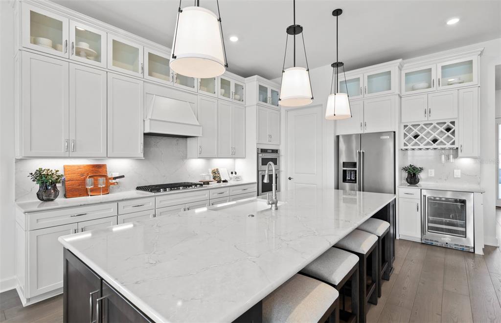 A modern kitchen features white cabinetry, a large marble island, and stainless steel appliances — 4933 DEL REY COVE, LAKEWOOD RANCH, FL