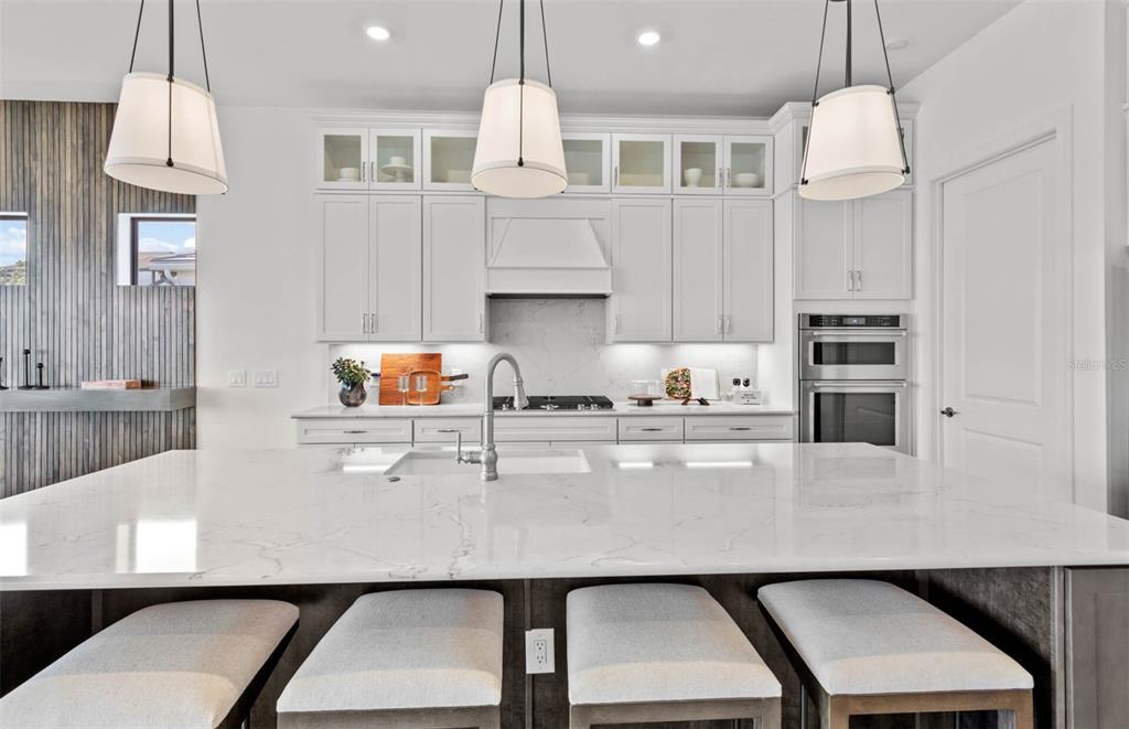 A modern kitchen features white cabinetry, a marble-topped island with bar stools, and pendant lighting — 4933 DEL REY COVE, LAKEWOOD RANCH, FL
