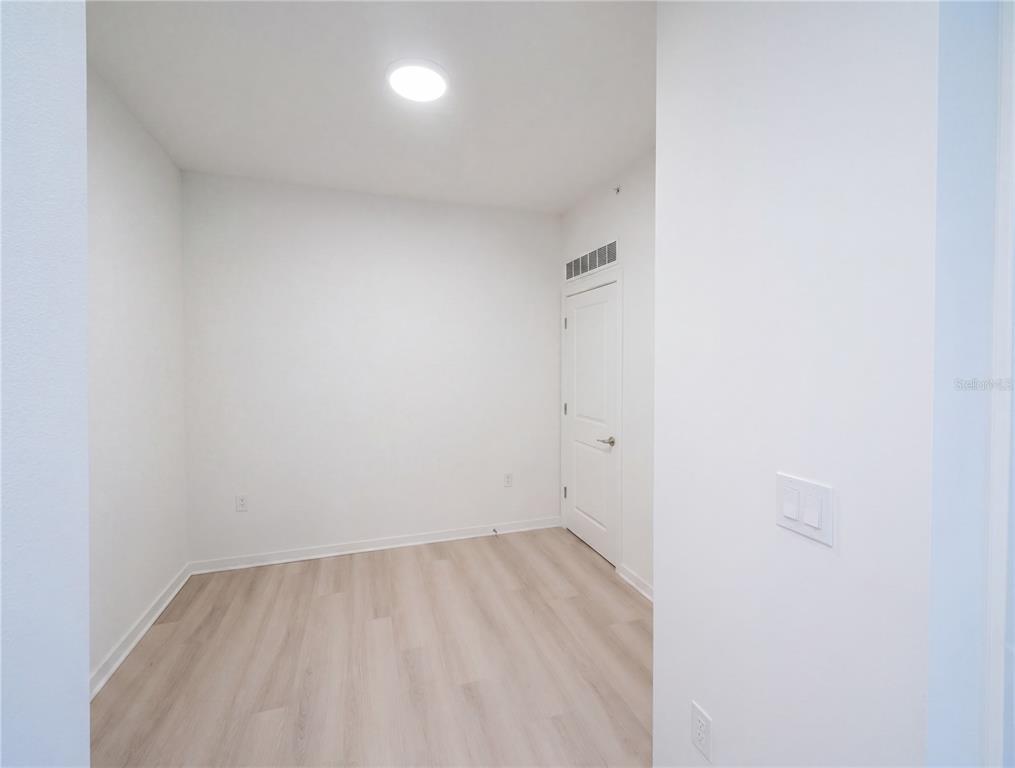 An empty room with white walls, light wood-look flooring, and a single closed door — 5579 MILLENIA PARK BOULEVARD UNIT 217, ORLANDO, FL