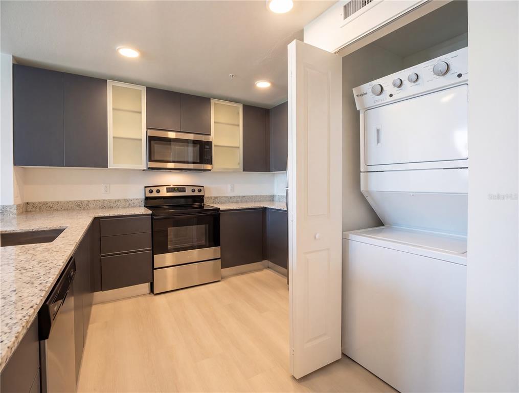 A kitchen with dark gray cabinets, granite countertops, and a stacked washer and dryer unit — 5579 MILLENIA PARK BOULEVARD UNIT 217, ORLANDO, FL