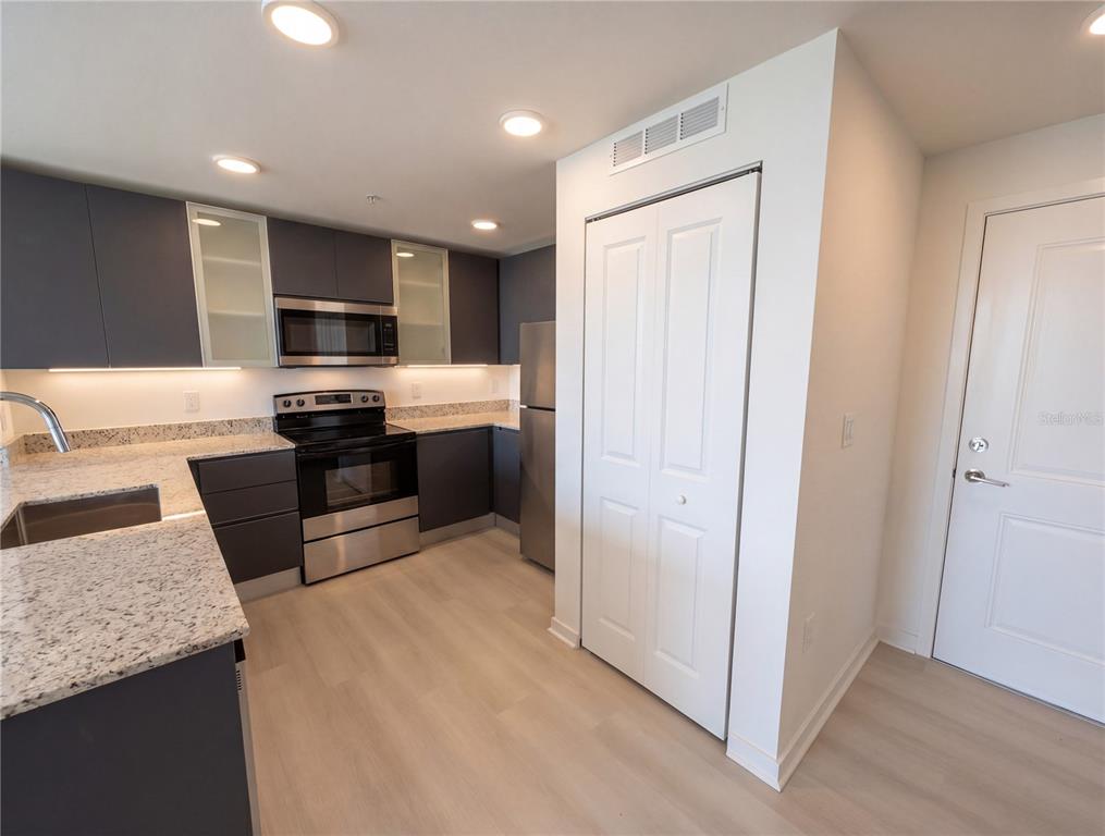 A modern kitchen features dark cabinetry, granite countertops, stainless steel appliances, and light wood flooring — 5579 MILLENIA PARK BOULEVARD UNIT 217, ORLANDO, FL