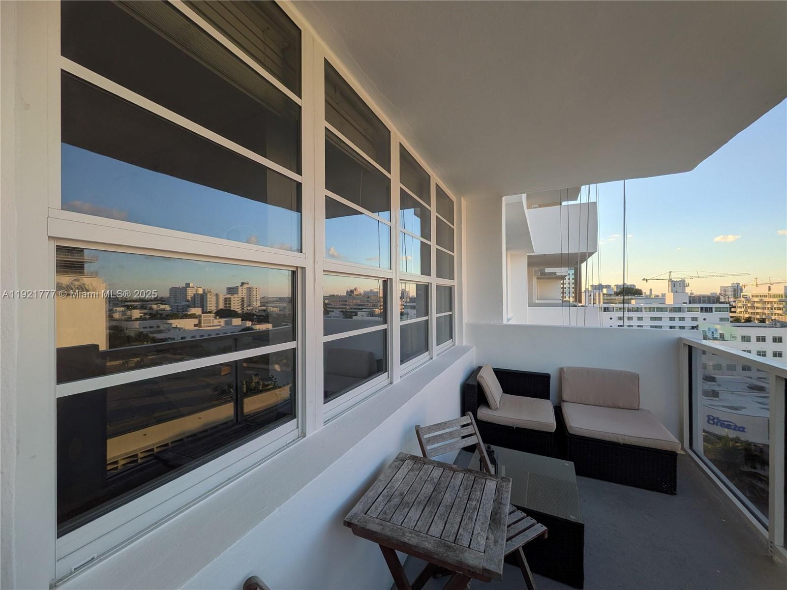 A balcony features a small wooden table, two chairs, and a view of city buildings — 100 Lincoln Rd # 904, Miami Beach FL 33139, MIAMI BEACH, FL