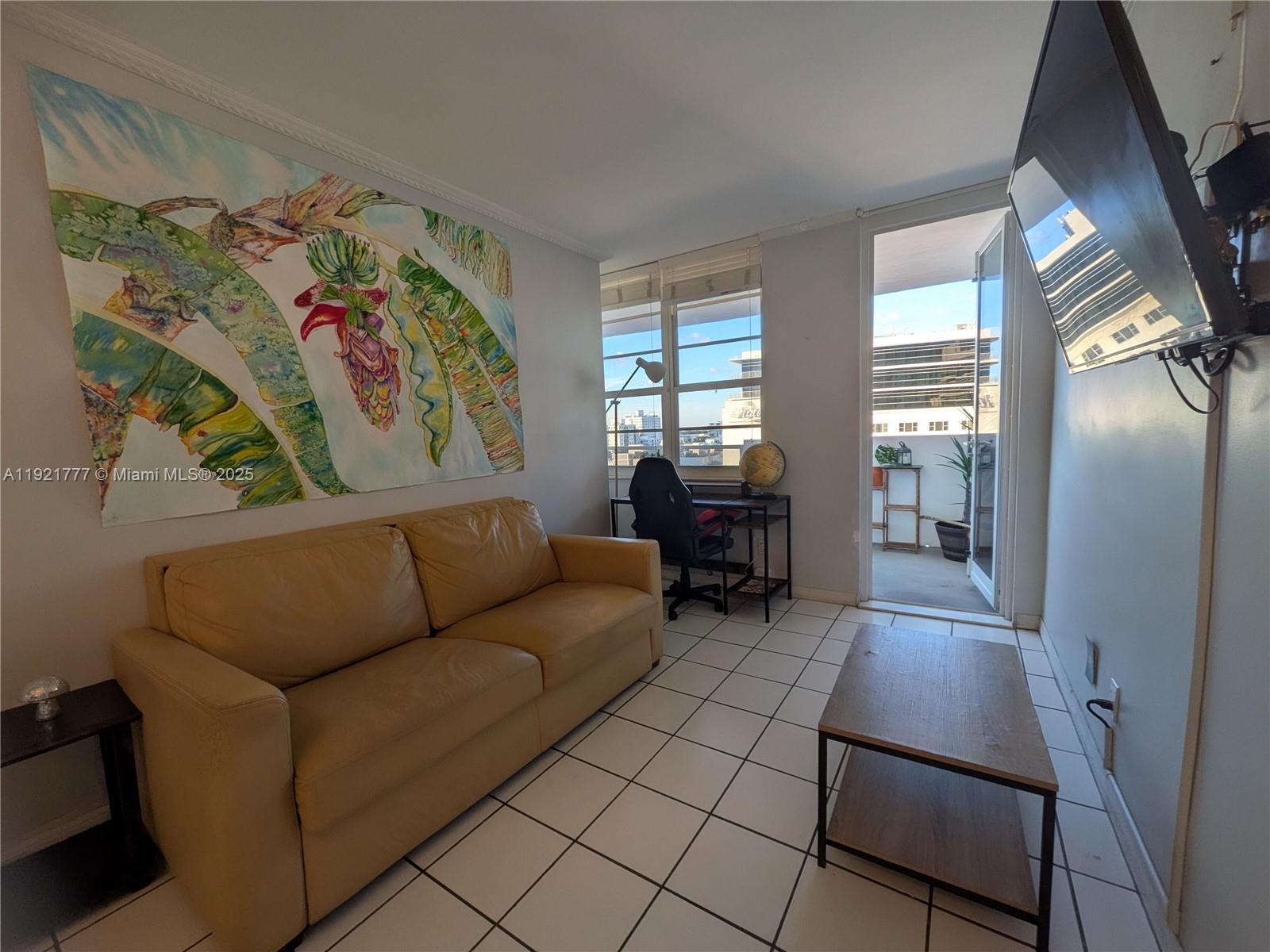 A living room features a tan sofa, a coffee table, a desk, and a balcony door — 100 Lincoln Rd # 904, Miami Beach FL 33139, MIAMI BEACH, FL