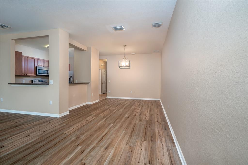 An open-concept dining area features light wood-look flooring and a view into the kitchen — 7818 BALLY MONEY ROAD, TAMPA, FL