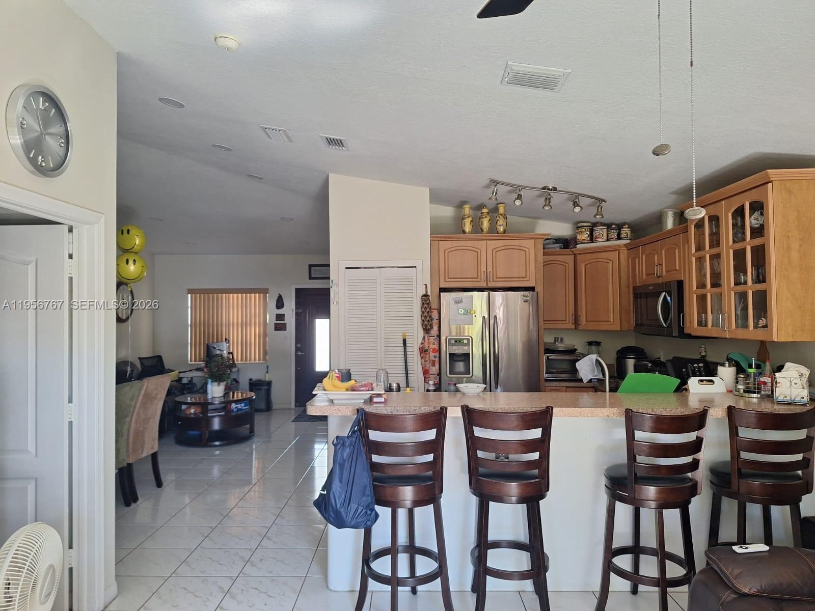 A kitchen with wooden cabinets and a breakfast bar overlooks an open-concept living area — 13822 SW 156th St, Miami FL 33177, MIAMI, FL