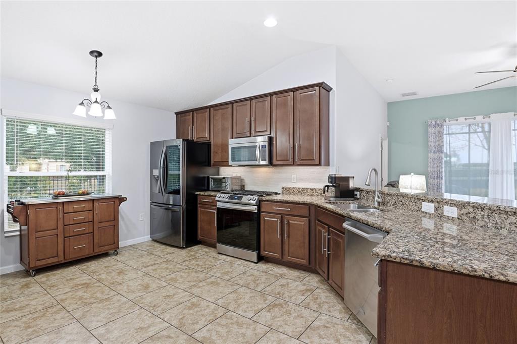A kitchen features brown cabinets, granite countertops, stainless steel appliances, and a rolling kitchen island — 476 SAUVIGNON WAY, GROVELAND, FL