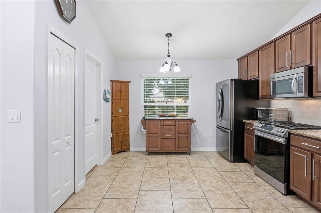 A kitchen with tile flooring, wooden cabinets, stainless steel appliances, and a windowed dining area — 476 SAUVIGNON WAY, GROVELAND, FL