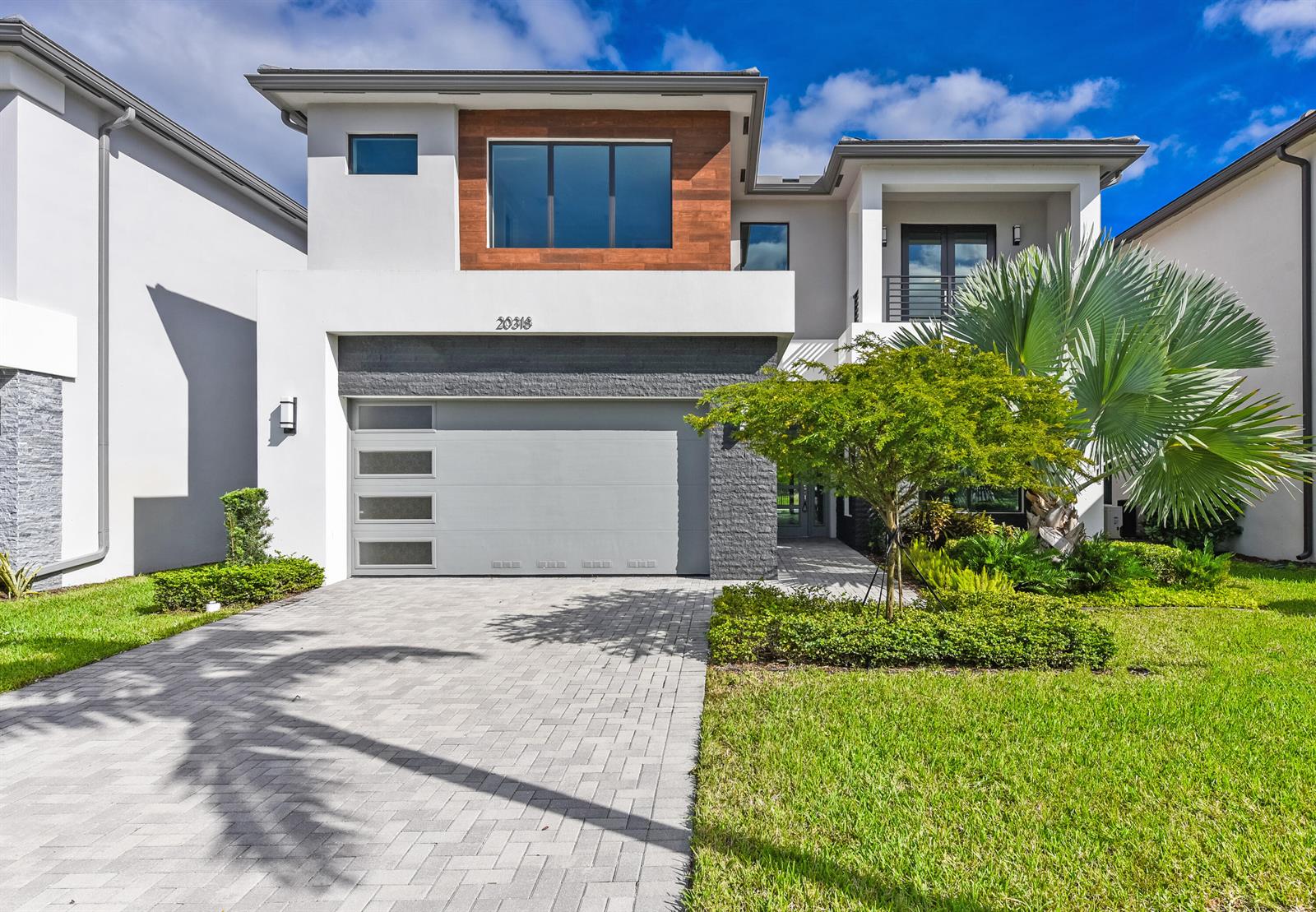A modern two-story house features a gray garage, wood-paneled accent wall, and a paved driveway — 20318 Castle Stuart Avenue, Boca Raton FL 33434, BOCA RATON, FL