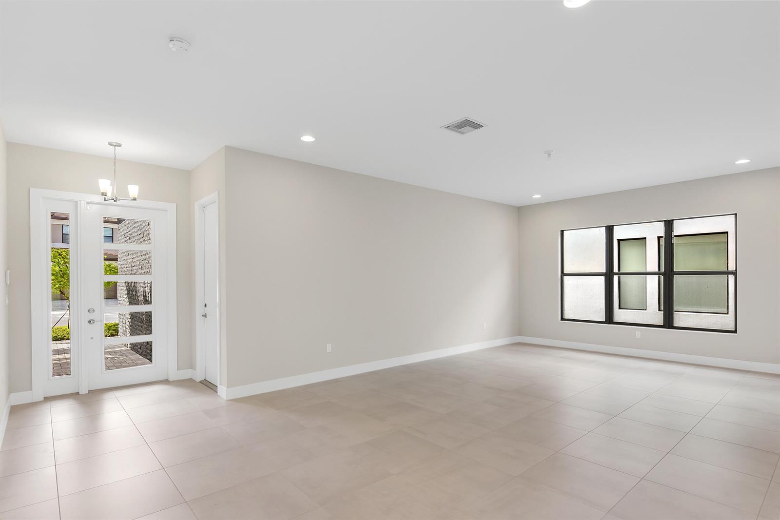 An empty room features light-colored tile floors, neutral walls, a glass-paneled front door, and windows — 20318 Castle Stuart Avenue, Boca Raton FL 33434, BOCA RATON, FL