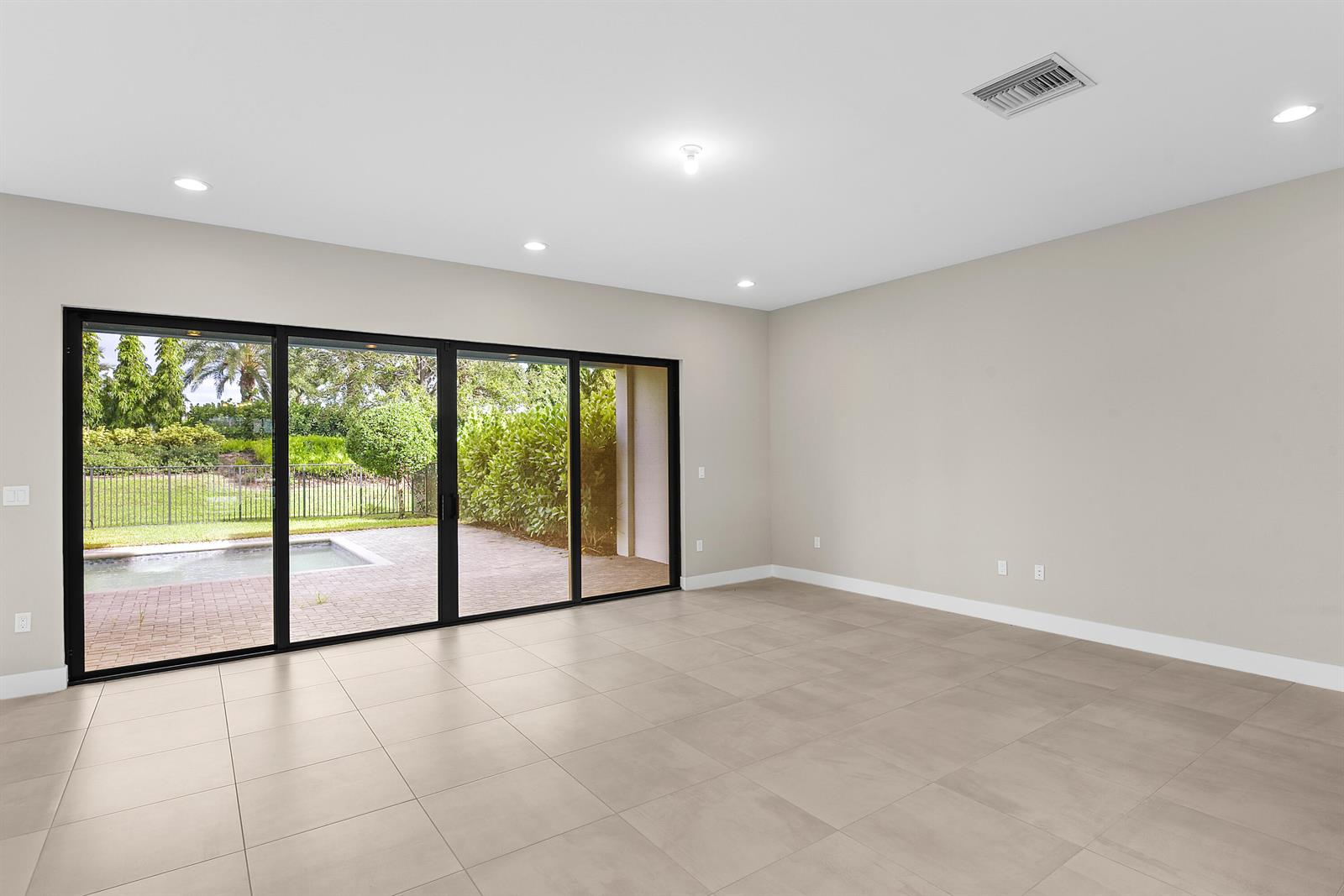 An empty room features large sliding glass doors opening to a patio and swimming pool — 20318 Castle Stuart Avenue, Boca Raton FL 33434, BOCA RATON, FL