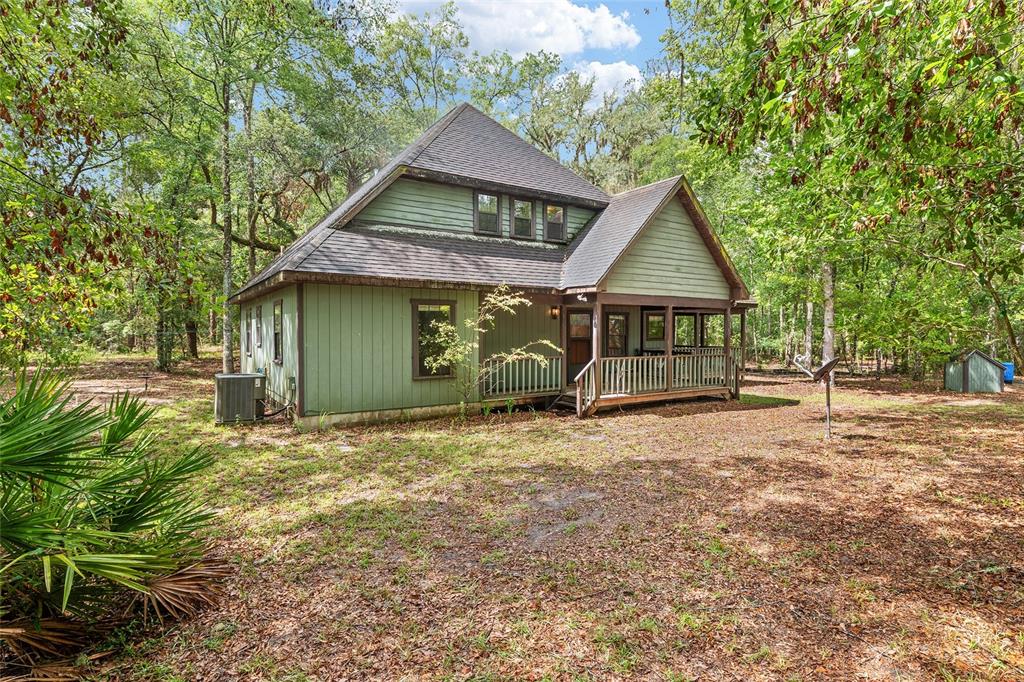 A green, two-story wooden house with a covered porch sits in a wooded yard — 7622 SE COUNTY ROAD 234, GAINESVILLE, FL