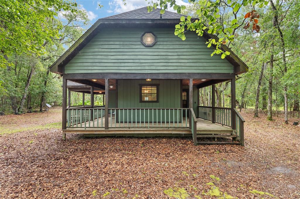 A green wooden cabin with a wraparound porch sits in a wooded area — 7622 SE COUNTY ROAD 234, GAINESVILLE, FL
