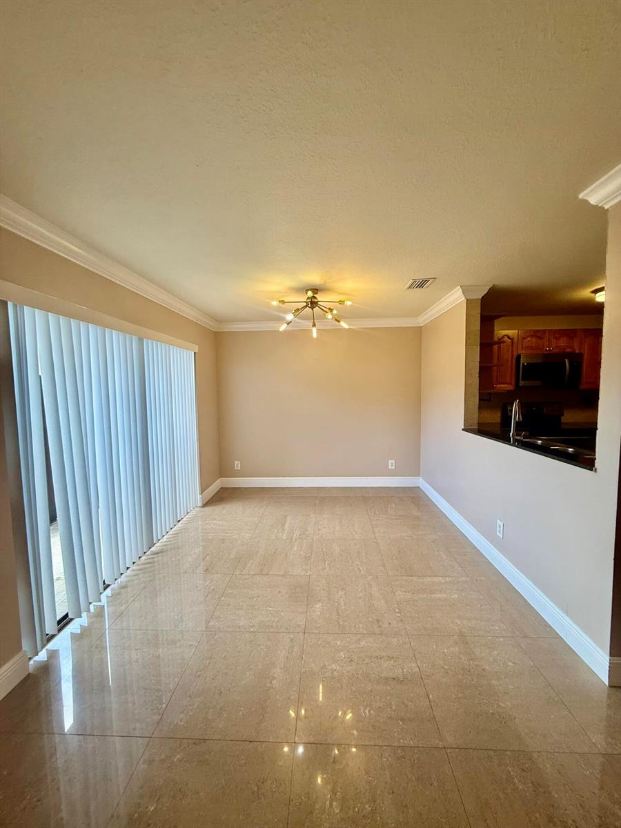 An empty dining area features beige tile flooring, crown molding, and a modern light fixture — 2050 Oleander Boulevard # 103, Fort Pierce FL 34950, FORT PIERCE, FL