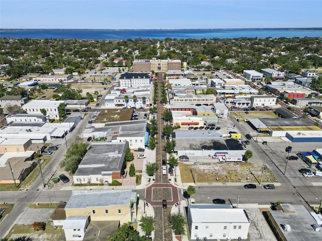 An aerial view shows a town street with commercial buildings leading toward a large lake — 1310 NEW YORK AVE, ST CLOUD, FL