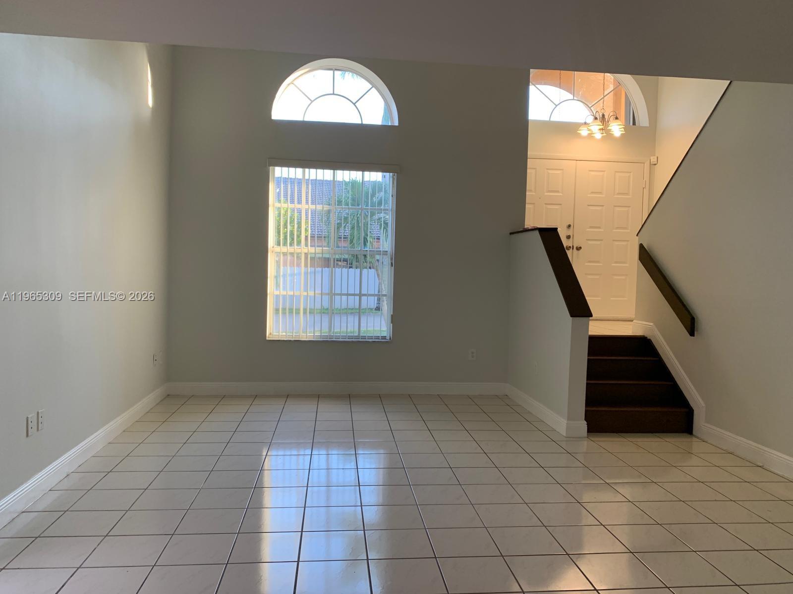 A bright living room features white tile floors, a large arched window, and a staircase — 12447 NW 7th St, Miami FL 33182, MIAMI, FL