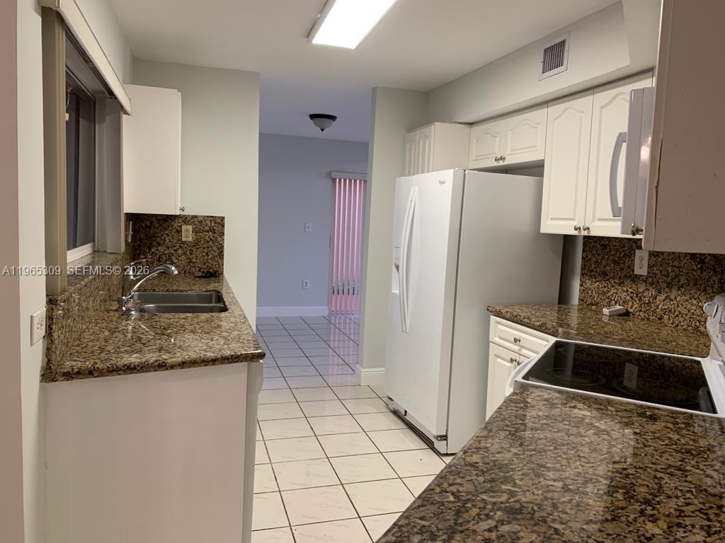 A kitchen features granite countertops, white cabinets, white appliances, and light-colored tile flooring — 12447 NW 7th St, Miami FL 33182, MIAMI, FL