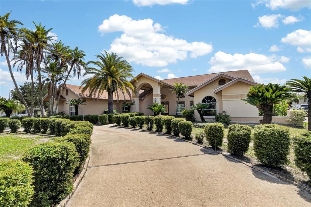 A beige house with a concrete driveway is lined by manicured hedges and palm trees — 2714 PINE CLUB DRIVE, PLANT CITY, FL
