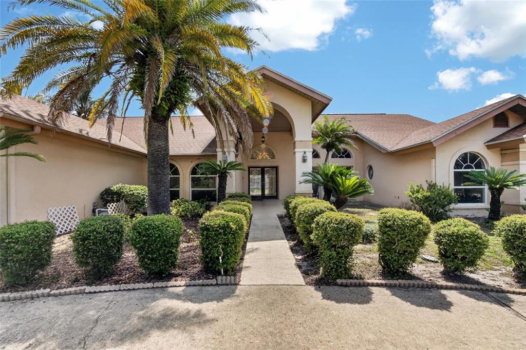 A beige house with a palm tree, manicured hedges, and a concrete walkway to the entrance — 2714 PINE CLUB DRIVE, PLANT CITY, FL
