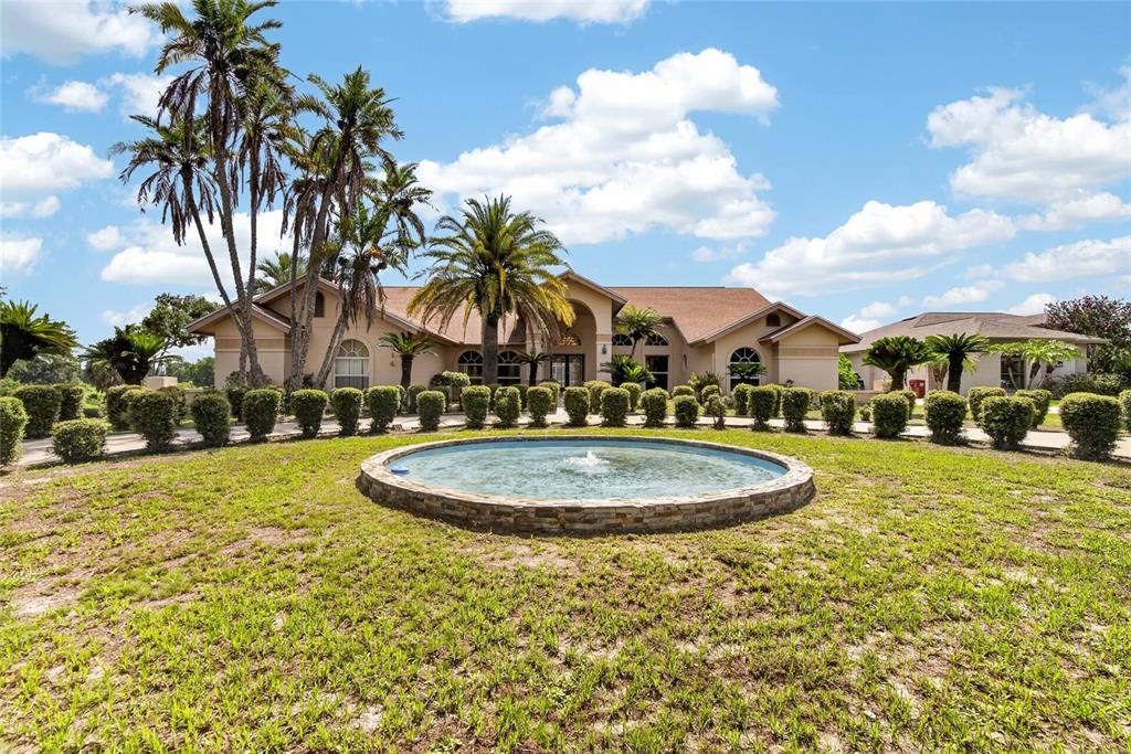 A circular stone fountain sits in the front yard of a large, single-story suburban home — 2714 PINE CLUB DRIVE, PLANT CITY, FL