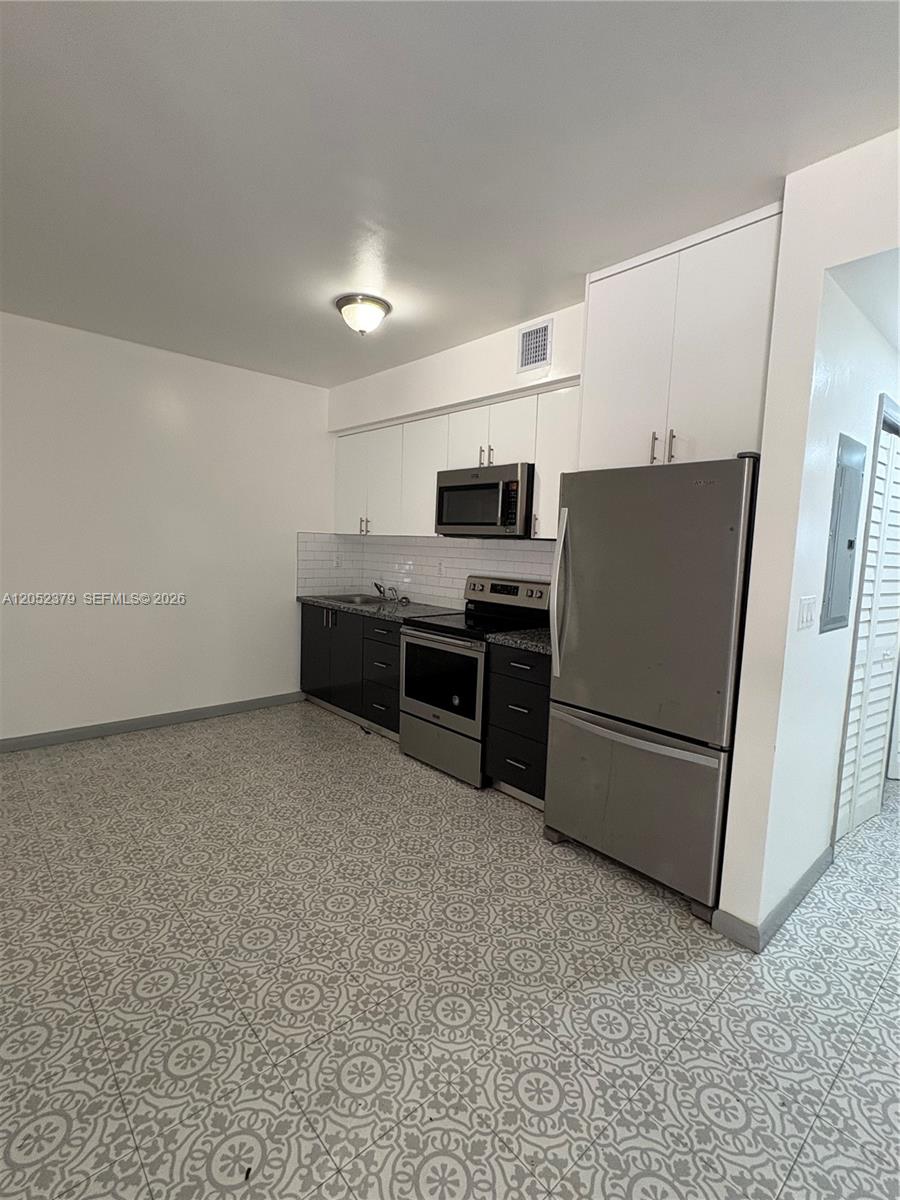 This kitchen features dark lower cabinets, white upper cabinets, stainless steel appliances, and patterned tile flooring — 10120 W Fern St, Miami FL 33157, MIAMI, FL