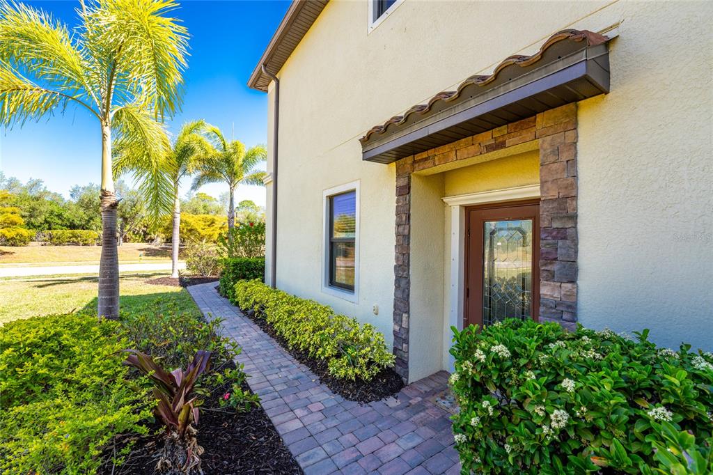 A paved walkway leads to a side entrance with a stone-trimmed doorway and awning — 20133 LAGENTE CIRCLE, VENICE, FL