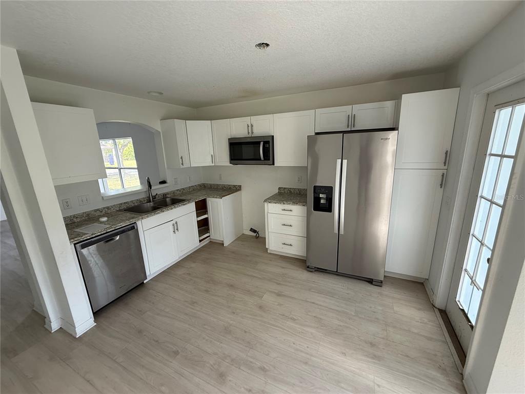A kitchen features white cabinets, stainless steel appliances, granite countertops, and light wood-look flooring — 4222 DAY BRIDGE PLACE UNIT 1400, ELLENTON, FL