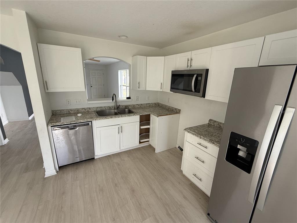 A kitchen features white cabinets, granite countertops, stainless steel appliances, and light wood-look flooring — 4222 DAY BRIDGE PLACE UNIT 1400, ELLENTON, FL