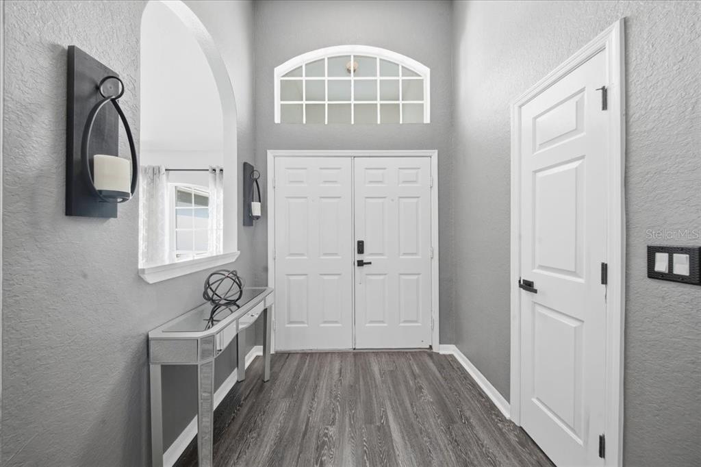 An entryway features a mirrored console table, gray walls, wood-look flooring, and double front doors — 1003 OLD CUTLER ROAD, LAKE WALES, FL