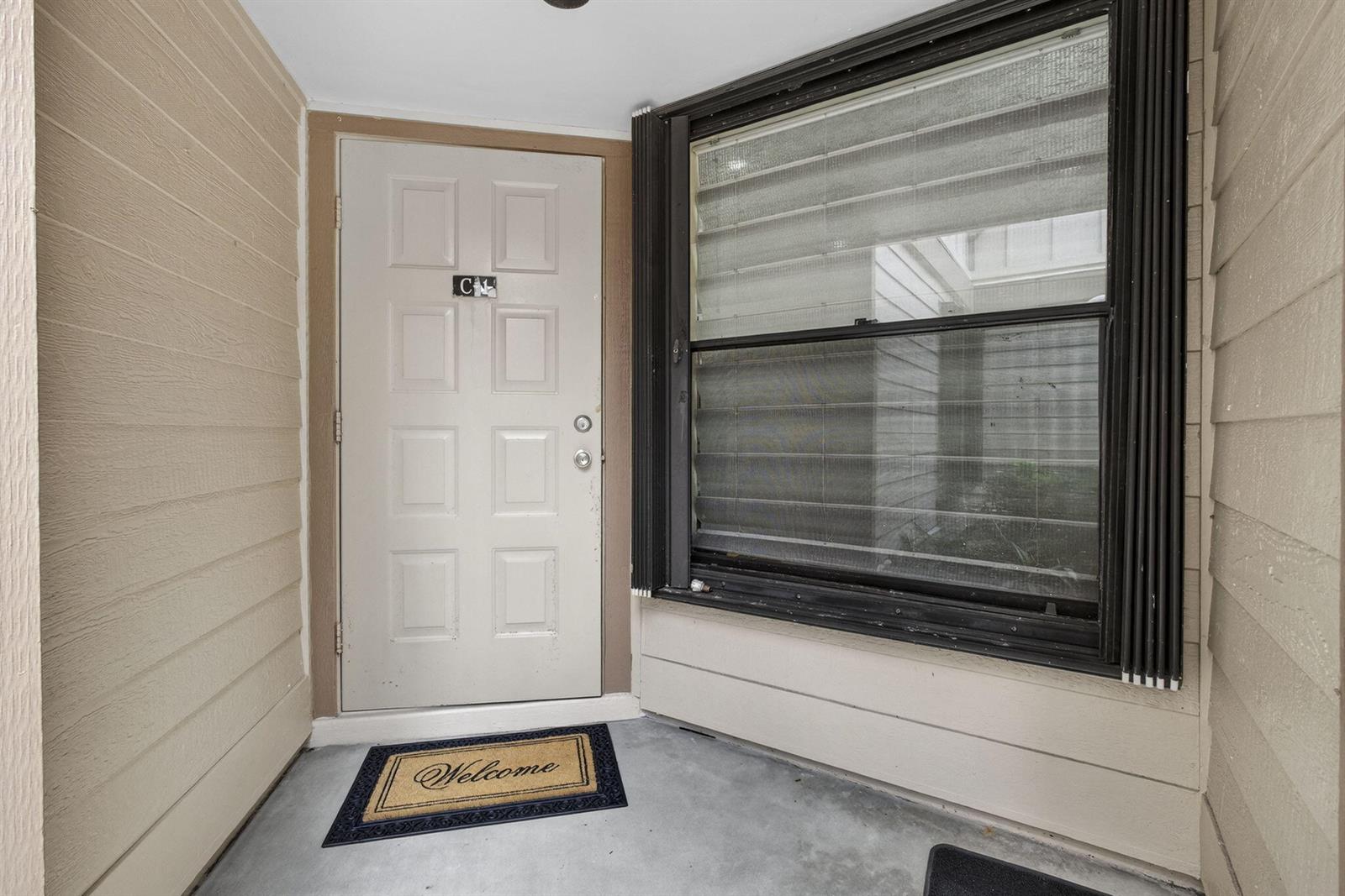 A beige front door with a welcome mat sits beside a large window with black trim — 500 Crosswinds Drive # C1, FL 33413, FL