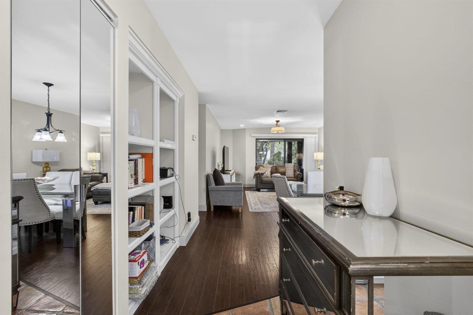 A hallway with dark wood floors leads to a living area with a mirrored wall — 500 Crosswinds Drive # C1, FL 33413, FL